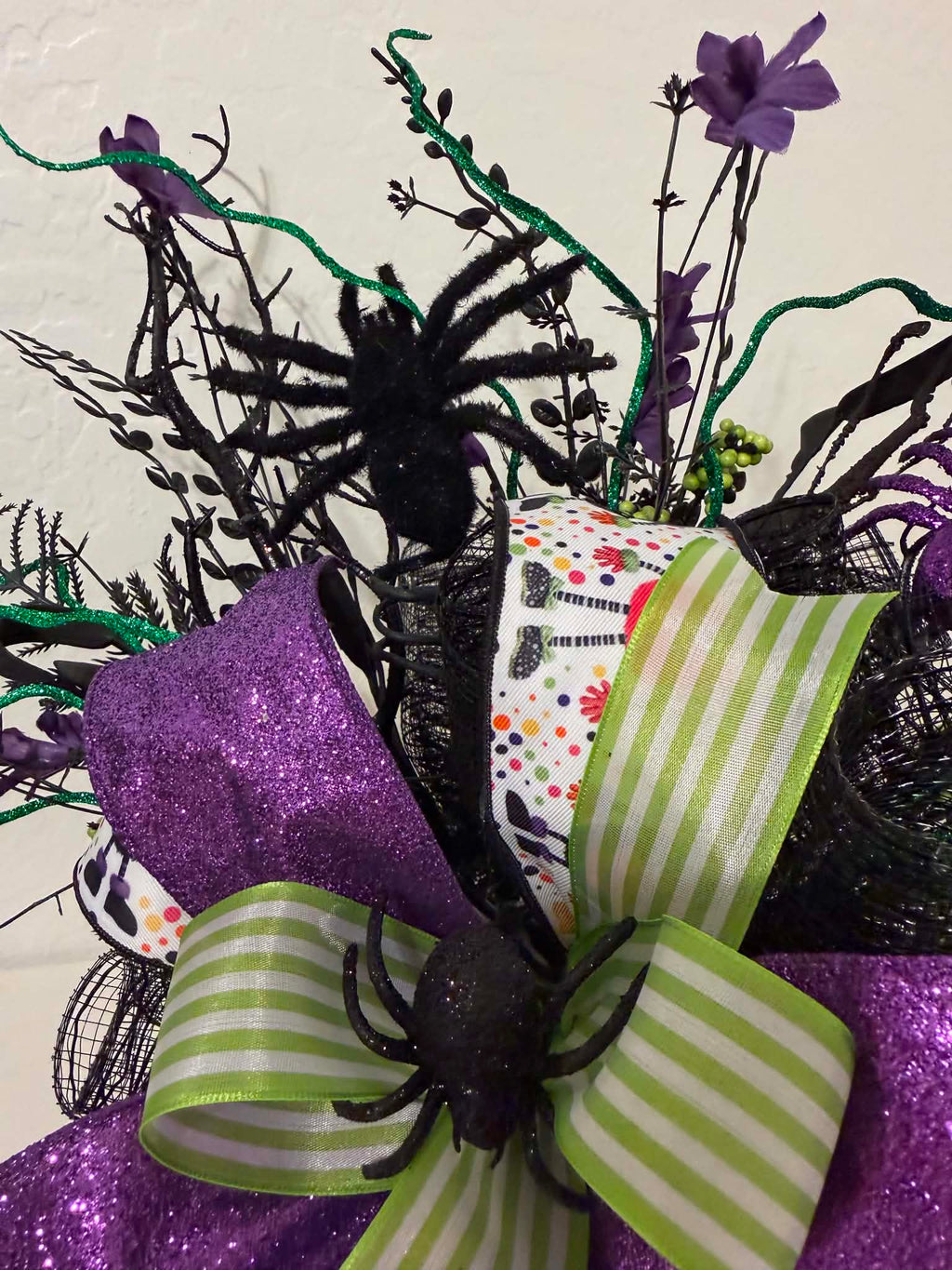 Close-up of purple glitter spider nestled in black branches and purple florals