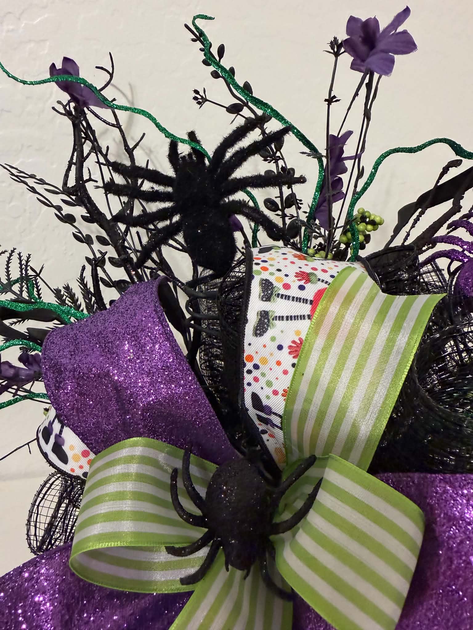 Close-up of purple glitter spider nestled in black branches and purple florals